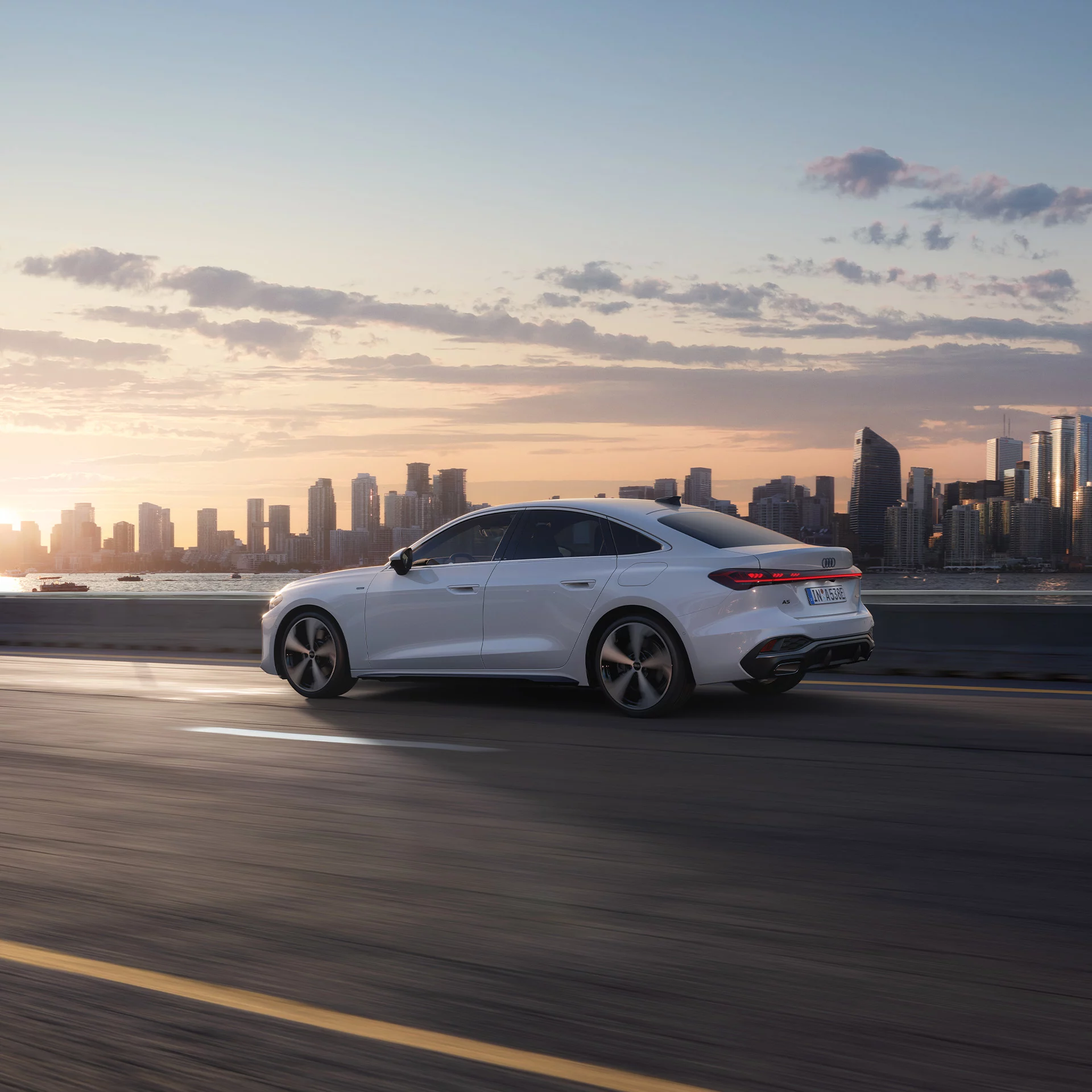 Audi A5 Limousine e-hybrid n einer Dynamischen Seitenansicht auf einer Straße mit einer Großstadt im Hintergrund 