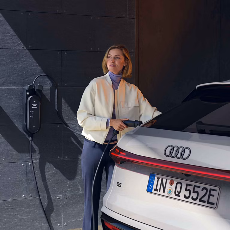 Audi Q5 Sportback e-hybrid Bei Laden an einem Haus mit einer Frau die ihn Lädt