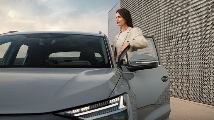 Oseba stoji ob odprtih vratih Audi Q4, pripravljena vstopiti. 