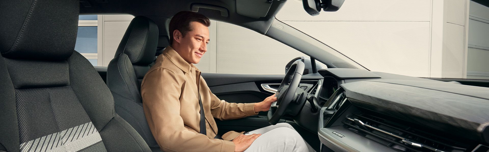 Oseba sedi za volanom avtomobila Audi Q4. Na sebi ima svetlo jakno in bele hlače. 