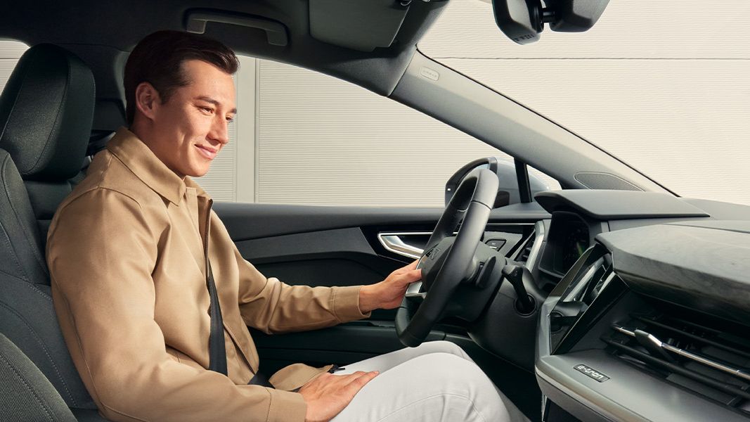 Oseba sedi za volanom avtomobila Audi Q4. Na sebi ima svetlo jakno in bele hlače. 