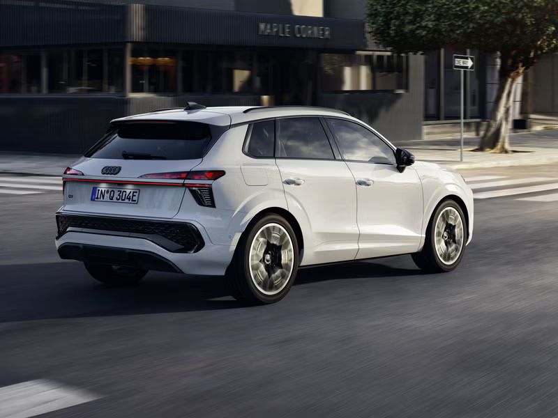 Ein weißer Q3 SUV e-hybrid von hinten rechts während der Fahrt an einer Straßenkreuzung in der Innenstadt.	