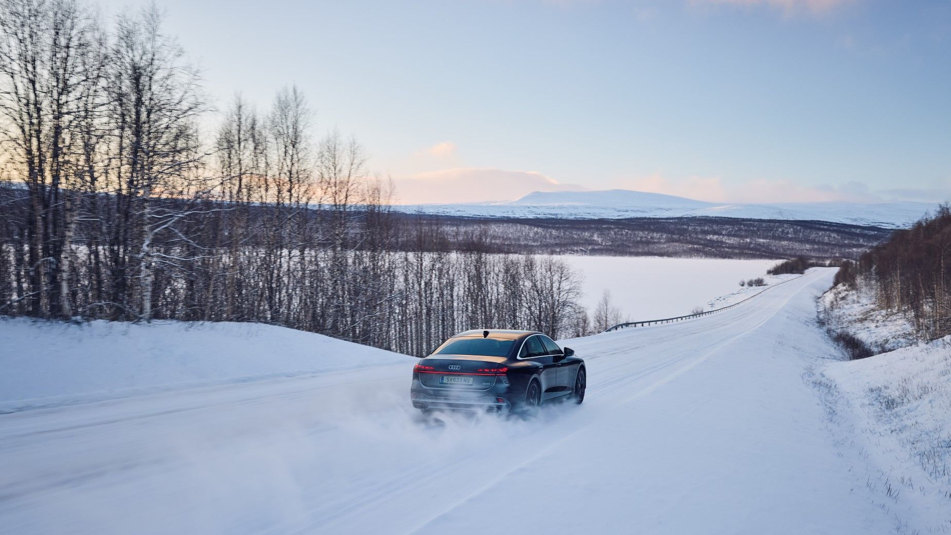 Ein Audi A6 in Heckansicht, fährt durch eine verschneite Winterlandschaft.