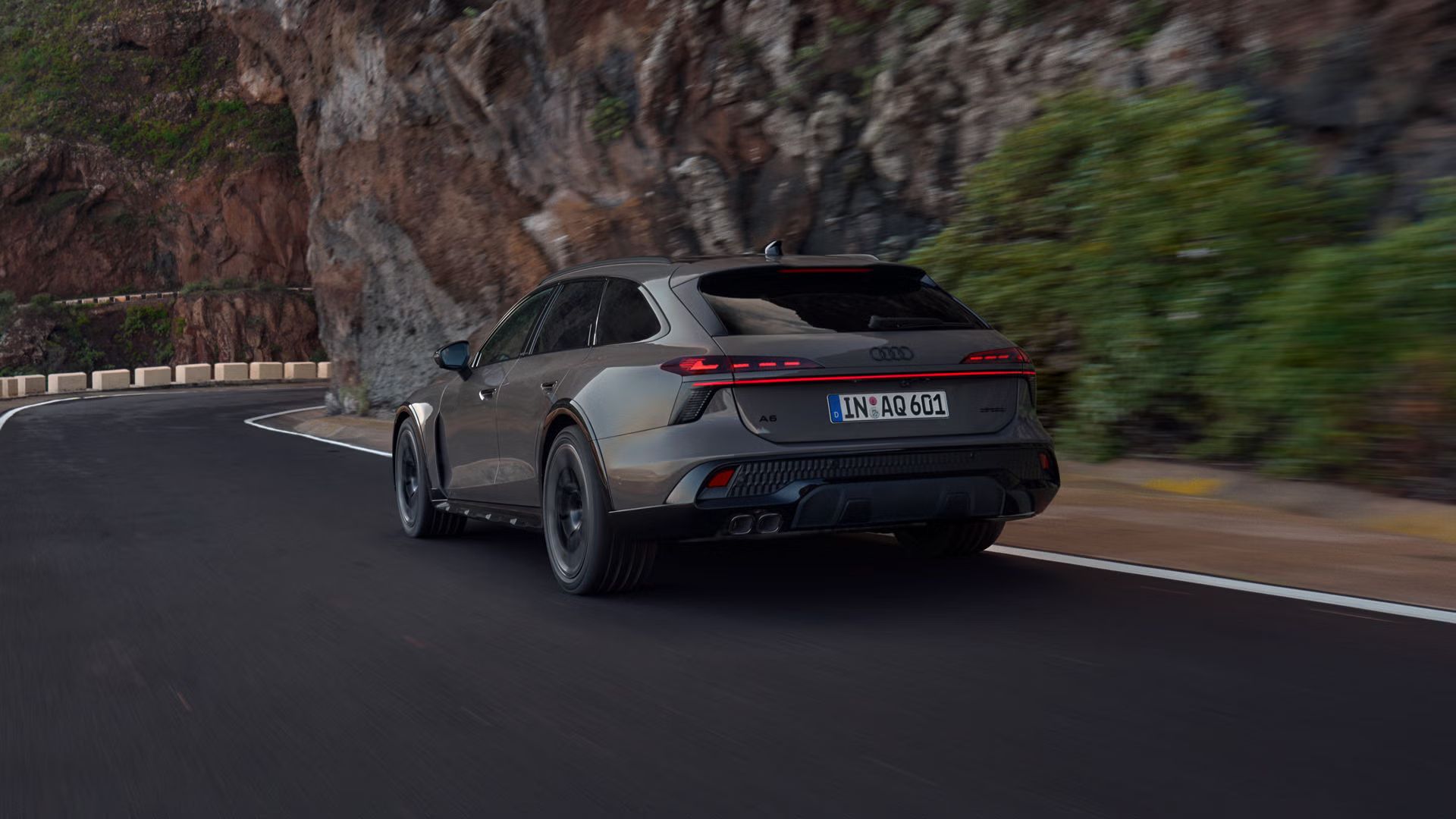 Audi A6 allraod, diagonalni pogled od zadaj, se pelje po gorski cesti. Na desni se dvigajo strme skalne stene.