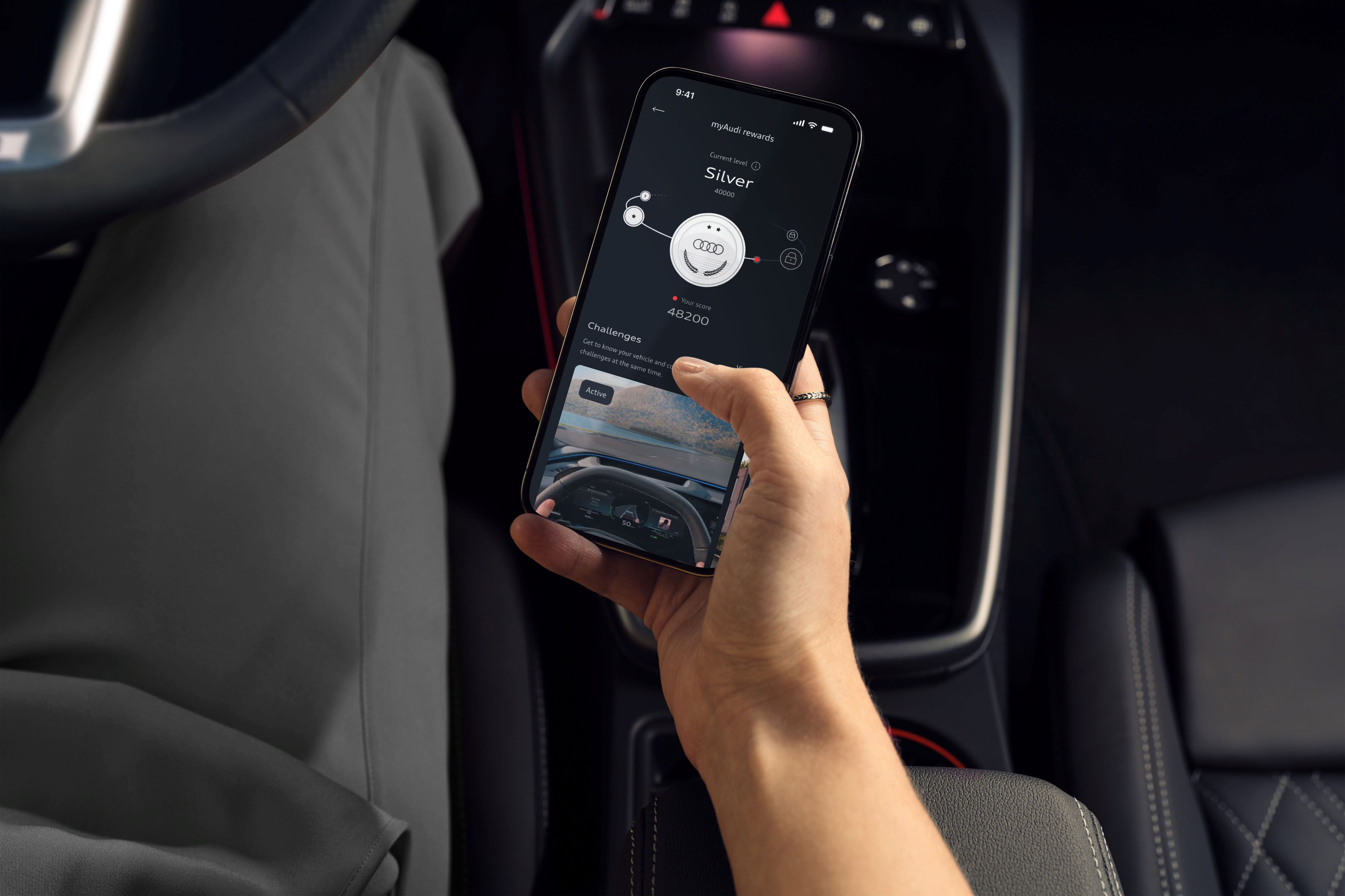 Oseba sedi na voznikovem sedežu Audi A3 in drži pametni telefon z odprto aplikacijo myAudi, povezano z vozilom. Na zaslonu so prikazane informacije o avtomobilu. Okolica prikazuje eleganten, temen in digitalen interier avtomobila z vidnim volanom in armaturno ploščo.