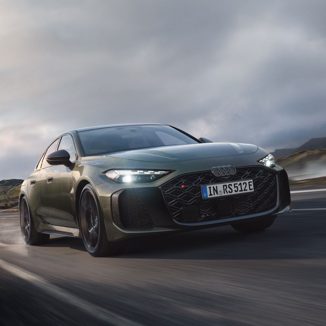 Audi RS 5 limuzina diagonalno od spredaj vozi po gorski cesti. Vodna para se dviga levo in desno.