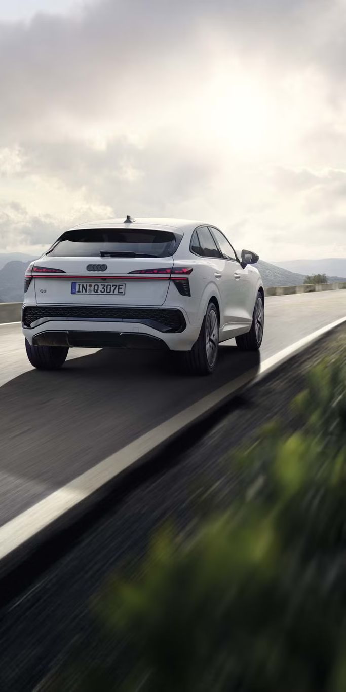 Ein weißer Q3 Sportback e-hybrid fährt auf einer Landstraße in einer bergigen Landschaft.	