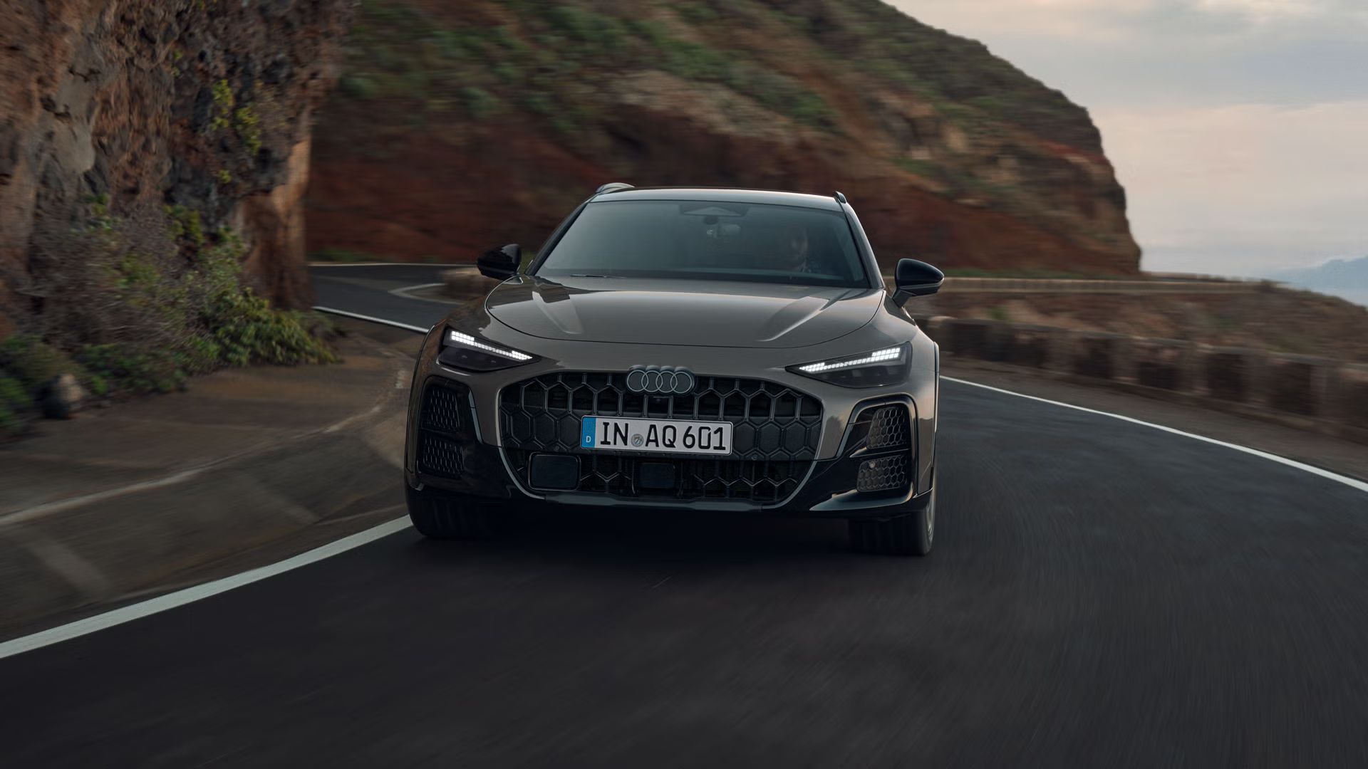 Audi A6 allroad od spredaj vozi po vijugasti gorski cesti. 