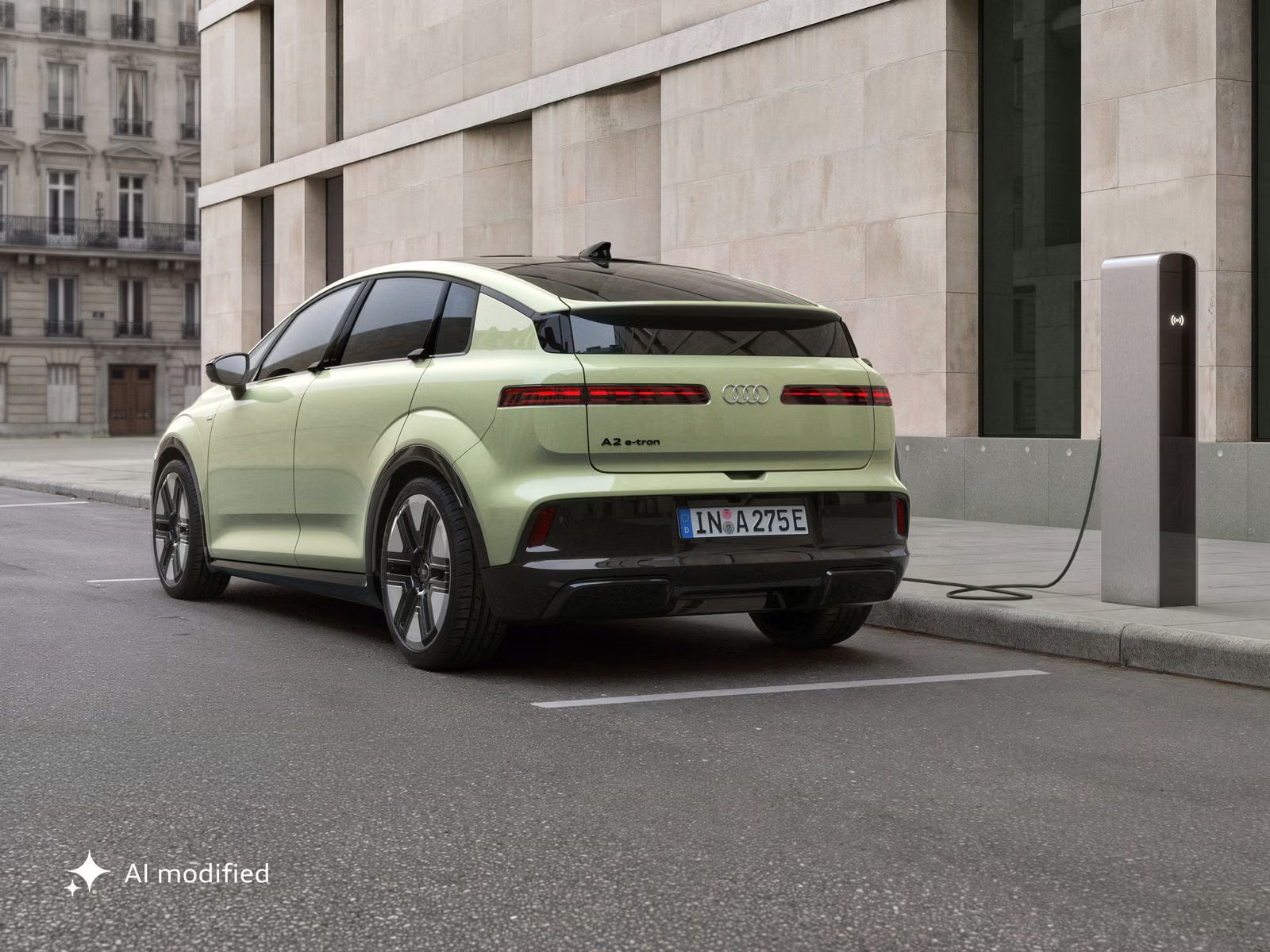 Stranski zadnji del vozila Audi A2 e-tron, parkiranega pred moderno stavbo. Vozilo je priključeno na polnilno postajo.