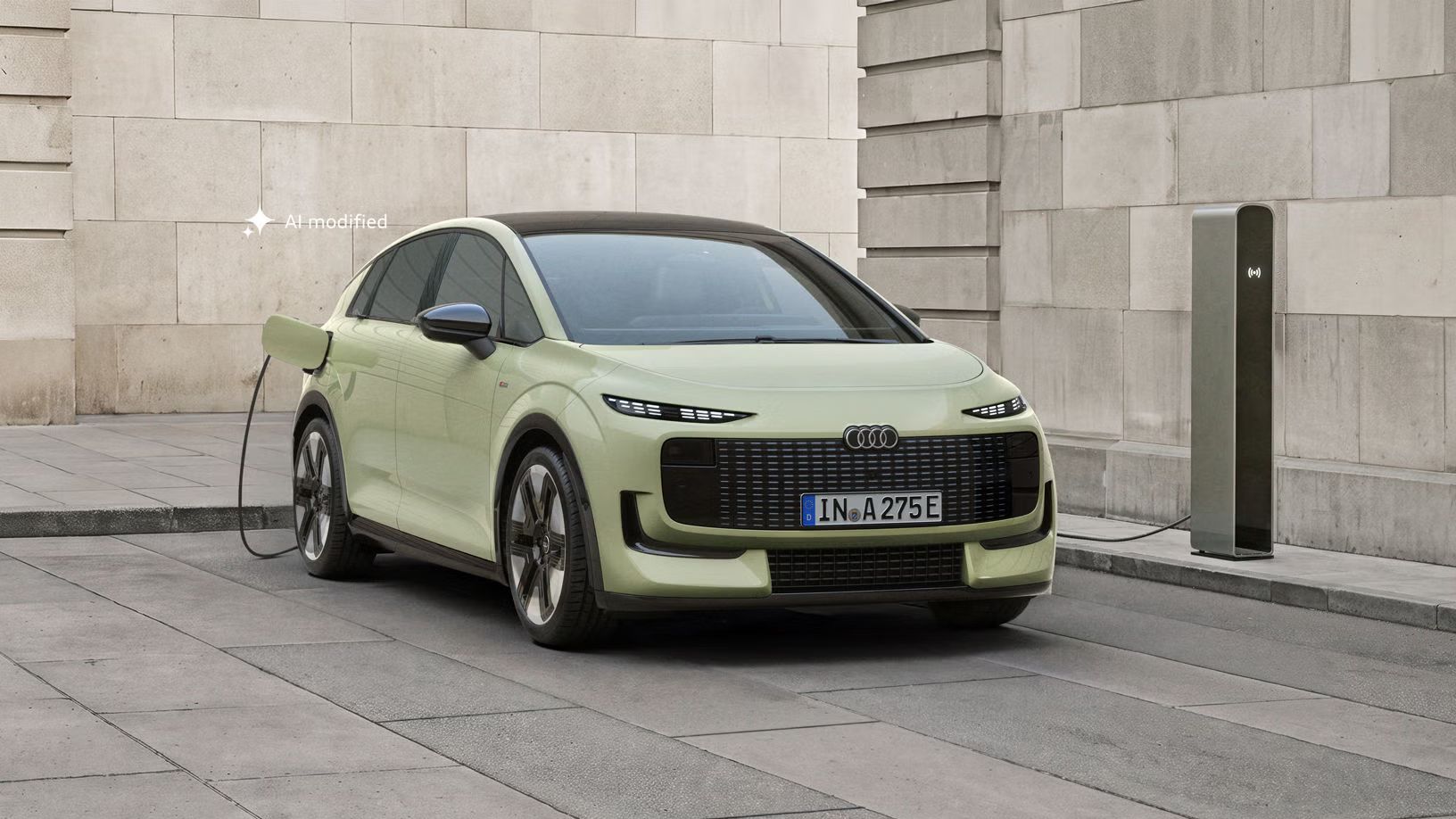 Audi A2 e-tron, fotografiran s sprednje strani, je parkiran pred moderno stavbo. Vozilo je priključeno na polnilno postajo.