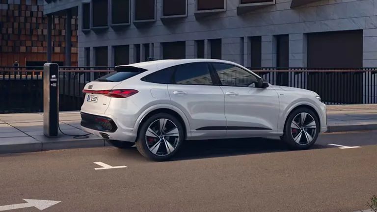 Audi Q5 Sportback e-hybrid se polni na polnilni postaji ob mestni ulici. 