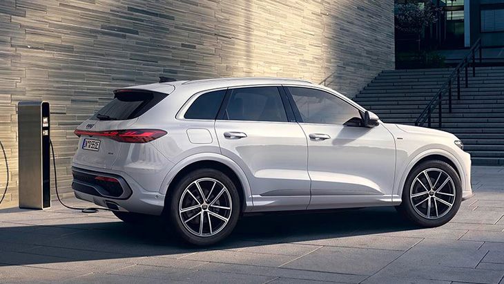 Audi Q5 parkiran pred zgradbo in priključen na polnilno postajo