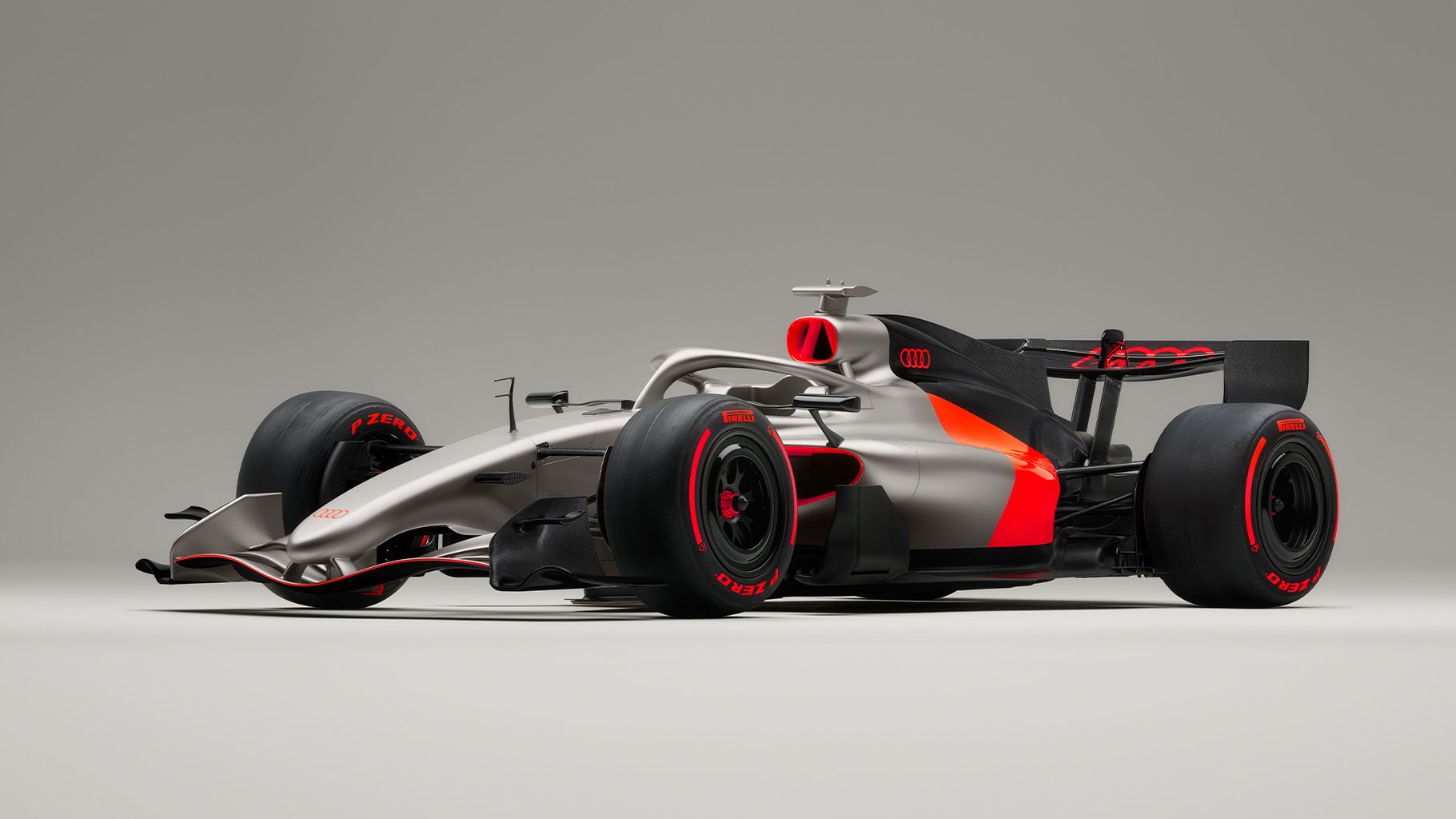 Audi F1®, osvetljen z leve strani, z aerodinamično oblikovano karoserijo in rdečimi trakovi na kolesih. 