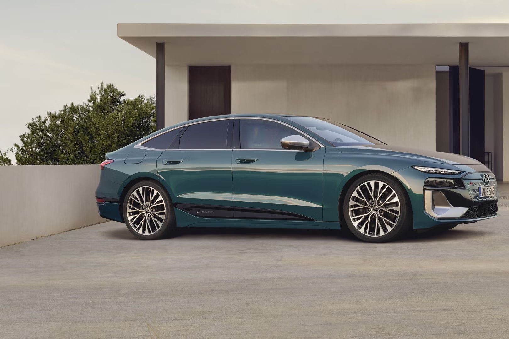 Električni Audi S6 e-tron je parkiran pred sodobno hišo in prikazan s strani. Vozilo stoji na urejenem dovozu v mirnem okolju. Poudarja čist dizajn in električno mobilnost znamke Audi.