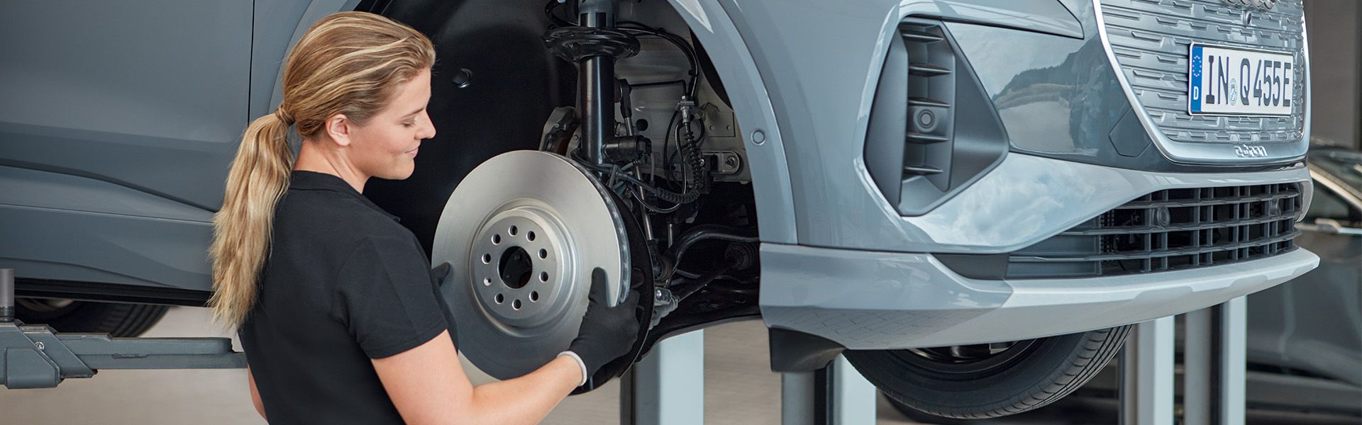 Preverjanje zavornega sistema avtomobila, ki je dvignjen na dvigalki v servisni delavnici. Avto ima nameščeno registrsko tablico.