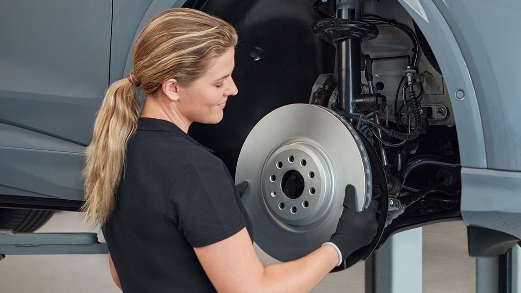 Preverjanje zavornega sistema avtomobila, ki je dvignjen na dvigalki v servisni delavnici. Avto ima nameščeno registrsko tablico.