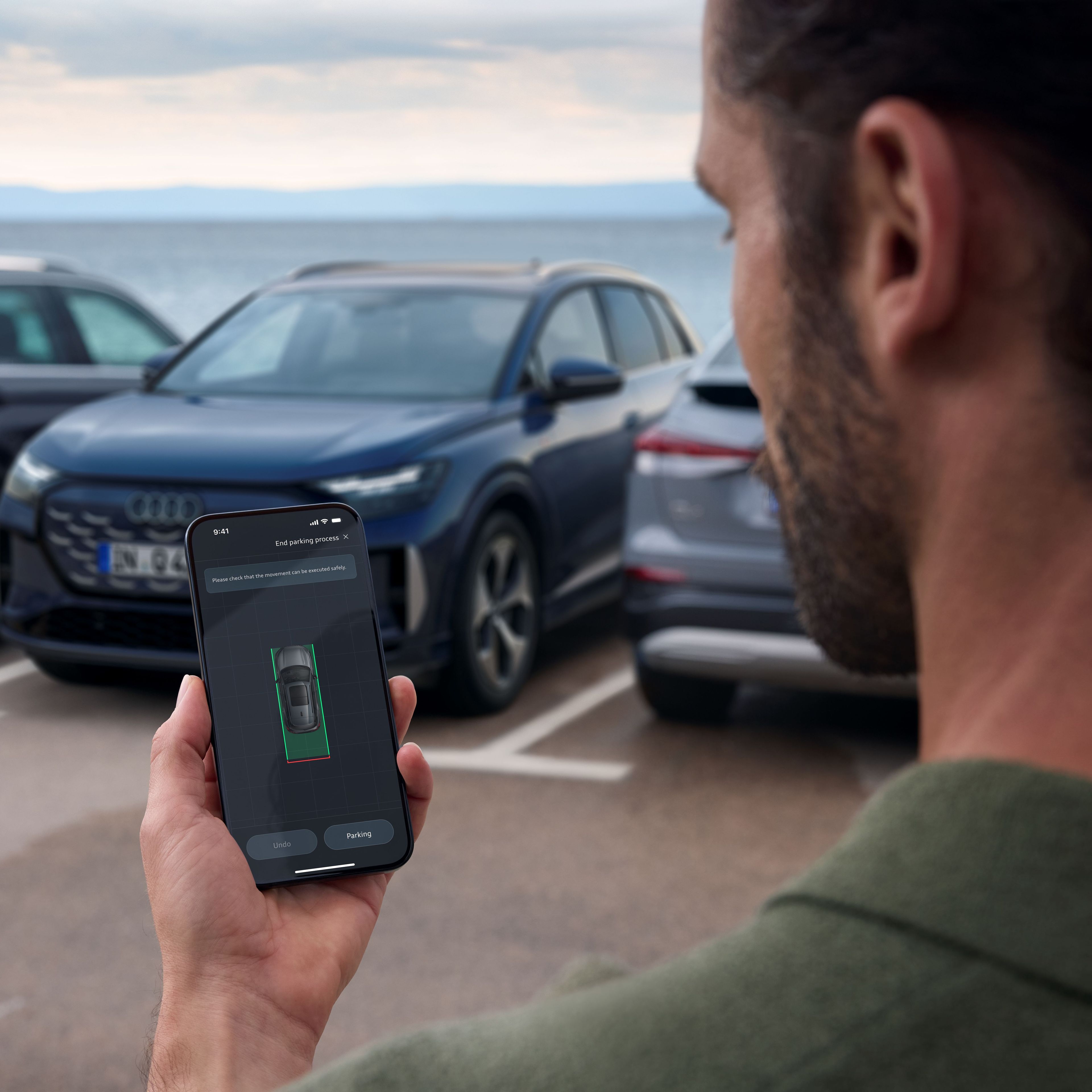 Voznik poleg parkiranega vozila Audi pregleduje aplikacijo myAudi