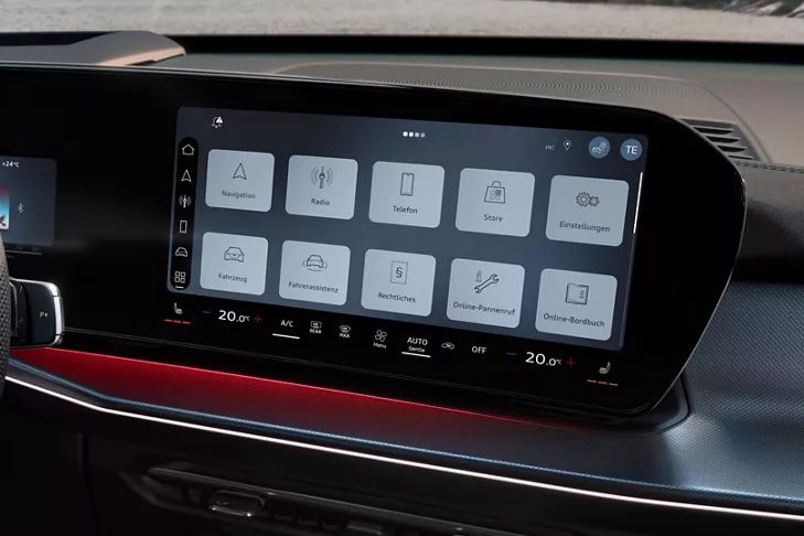 Notranjost avtomobila z velikim digitalnim zaslonom na armaturni plošči. Zaslon prikazuje različne ikone za navigacijo, radio, telefon in druge funkcije vozila. Voznikov sedež in del volana sta vidna v ospredju.