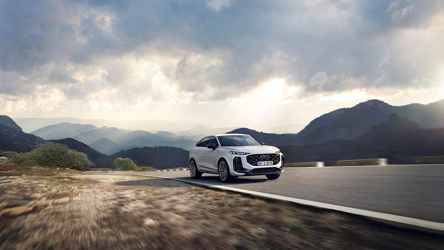 Beli Audi Q3 Sportback e-hybrid  se pelje po ovinkasti cesti v goratem območju ob oblačnem vremenu. 