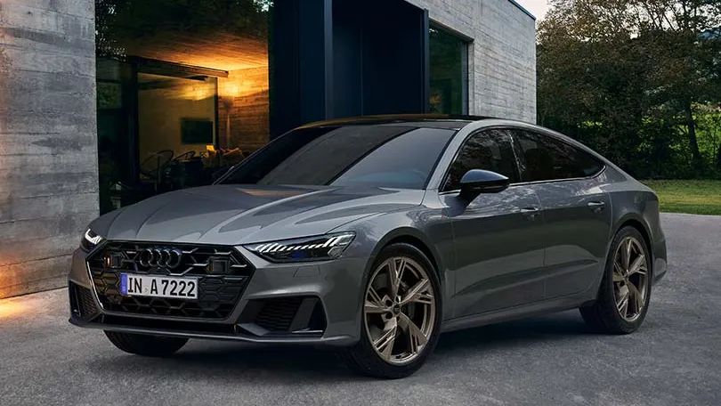 Na sliki je Audi A7, parkirana pred moderno hišo. 