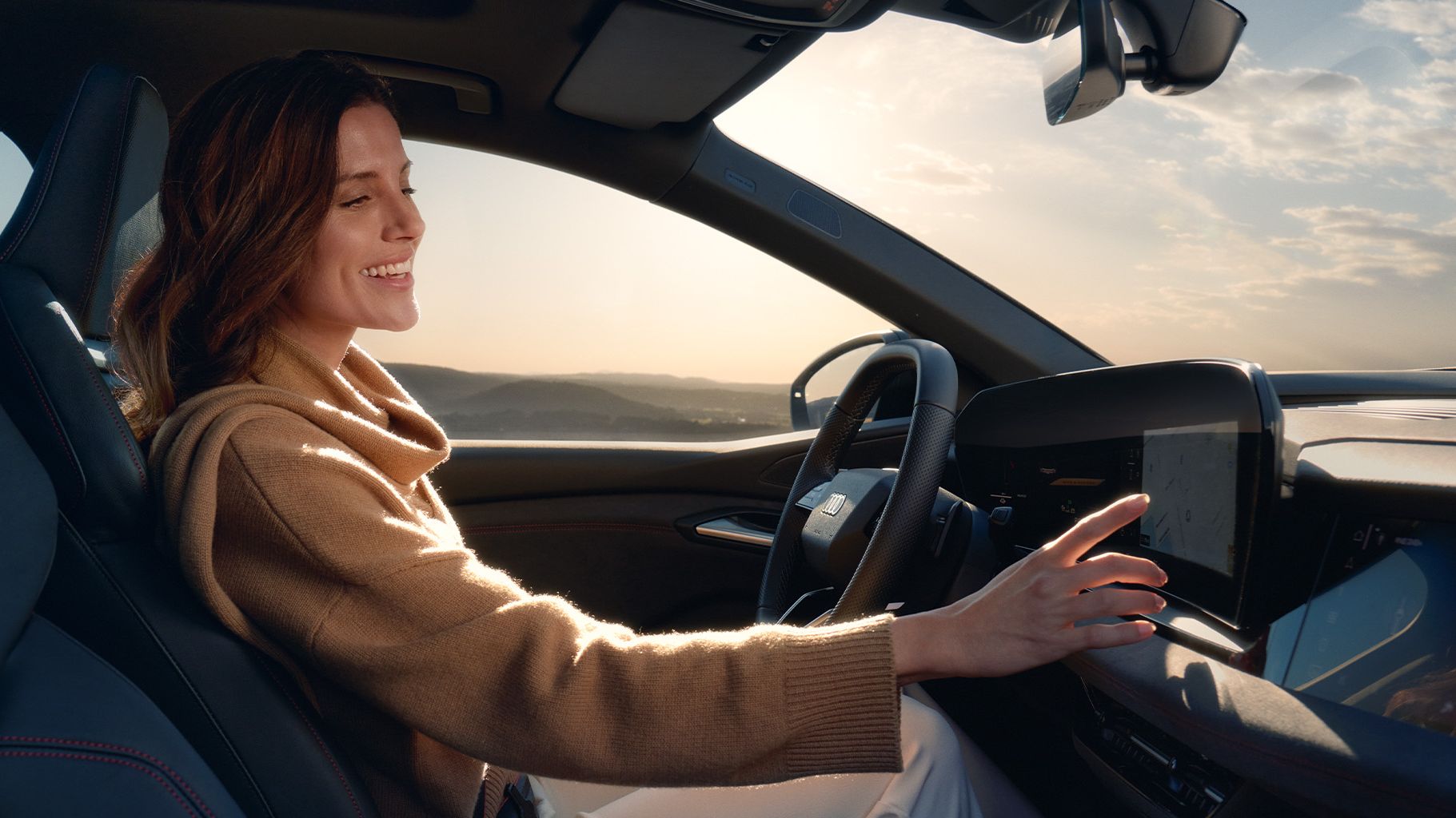 Ženska sedi na voznikovem sedežu Audi A5 in z roko upravlja zaslon na dotik na armaturni plošči.