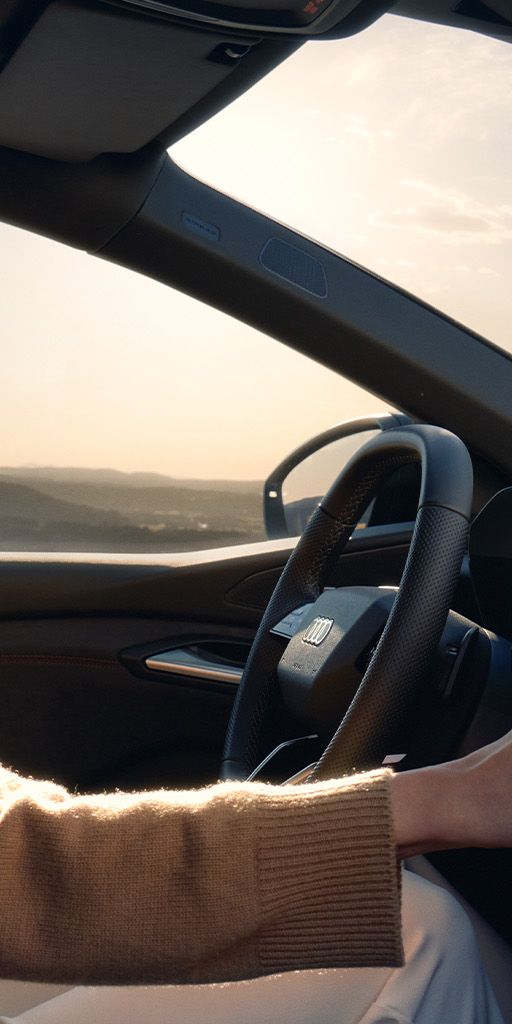 Ženska sedi na voznikovem sedežu Audi A5 in z roko upravlja zaslon na dotik na armaturni plošči.