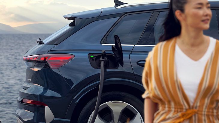 Bližnji posnetek zadnjega dela vozila Audi Q4 SUV e-tron in ženske. Vozilo je priključeno na javno polnilno postajo. 