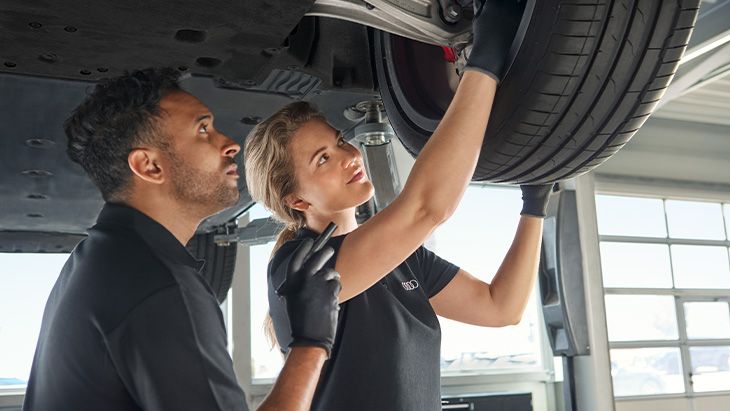 Dve osebi pod avtomobilom opravljata pregled zavore.