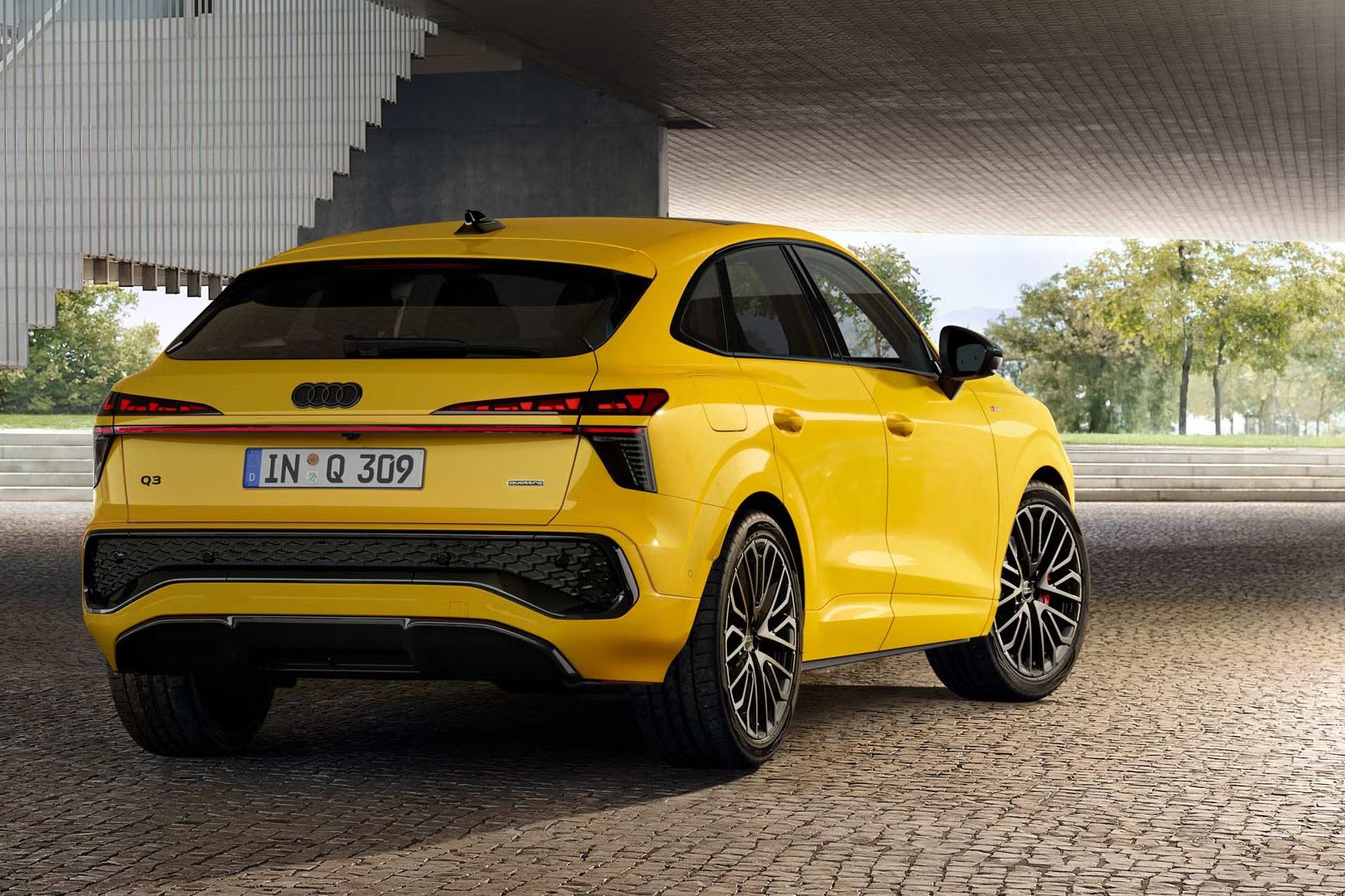 Rumeni Audi Q3 Sportback je parkiran na asfaltirani površini pred ograjo stopnišča.