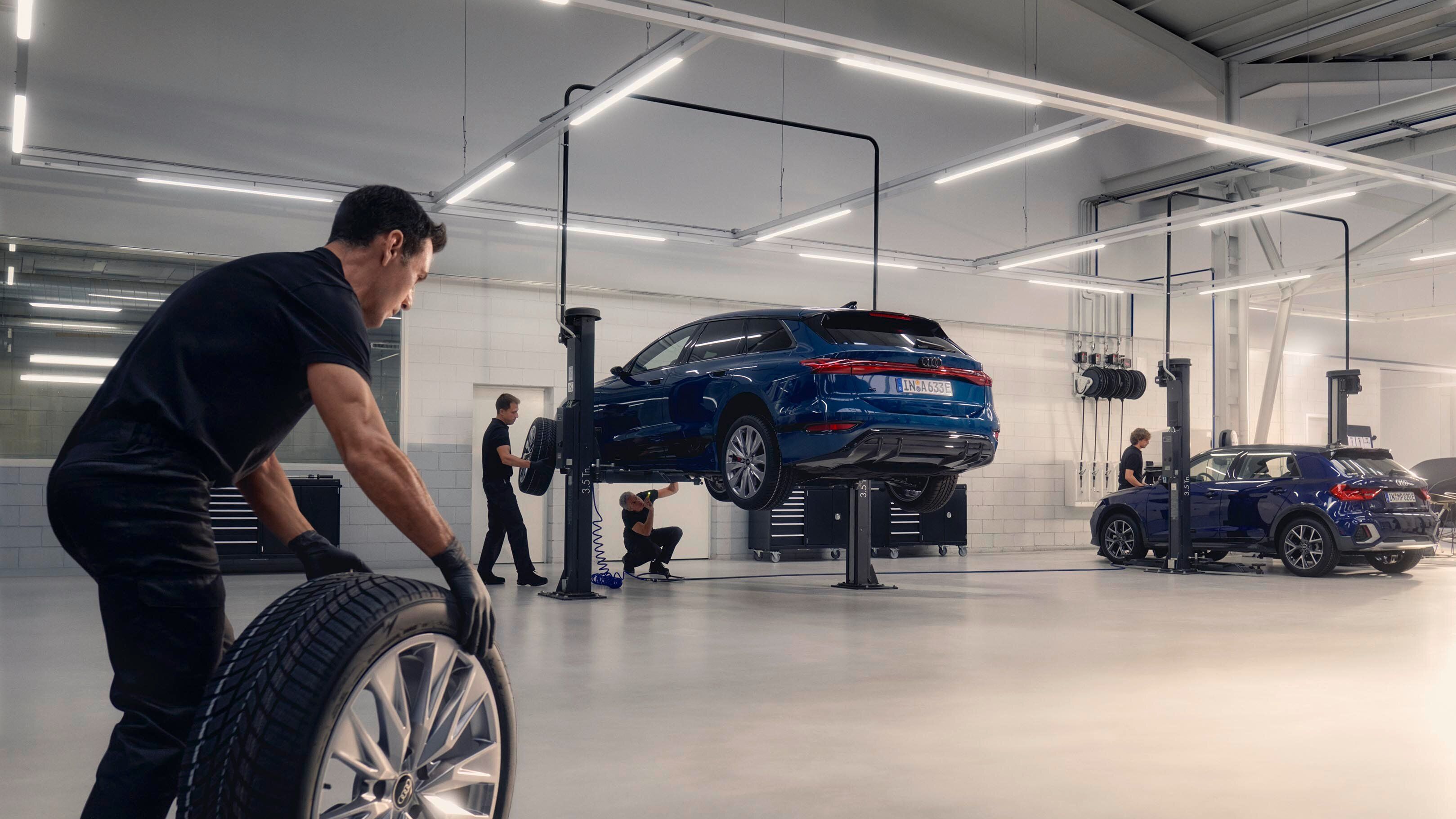 Ein Audi Mechaniker rollt ein Winterkomplettrad in Richtung eines Audi auf einer Hebebühne.