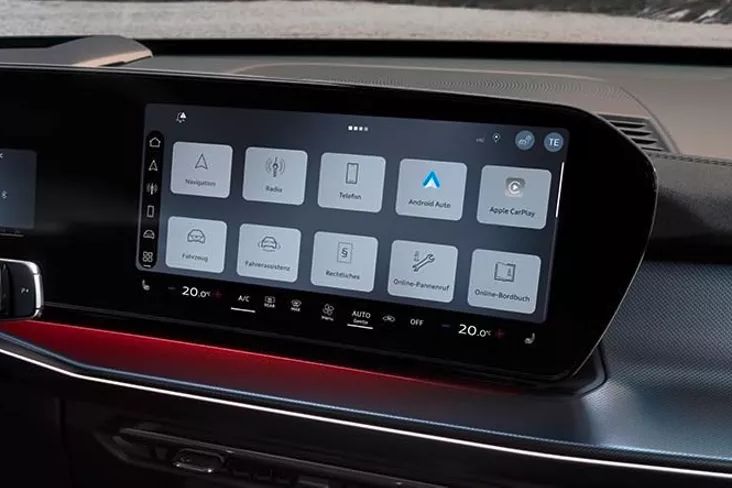 Notranjost Audi Q3 z velikim zaslonom na dotik na osrednji konzoli. Na zaslonu so prikazane različne aplikacije in funkcije vozila. V ozadju je vidna vetrobranska stekla z delom armaturne plošče.