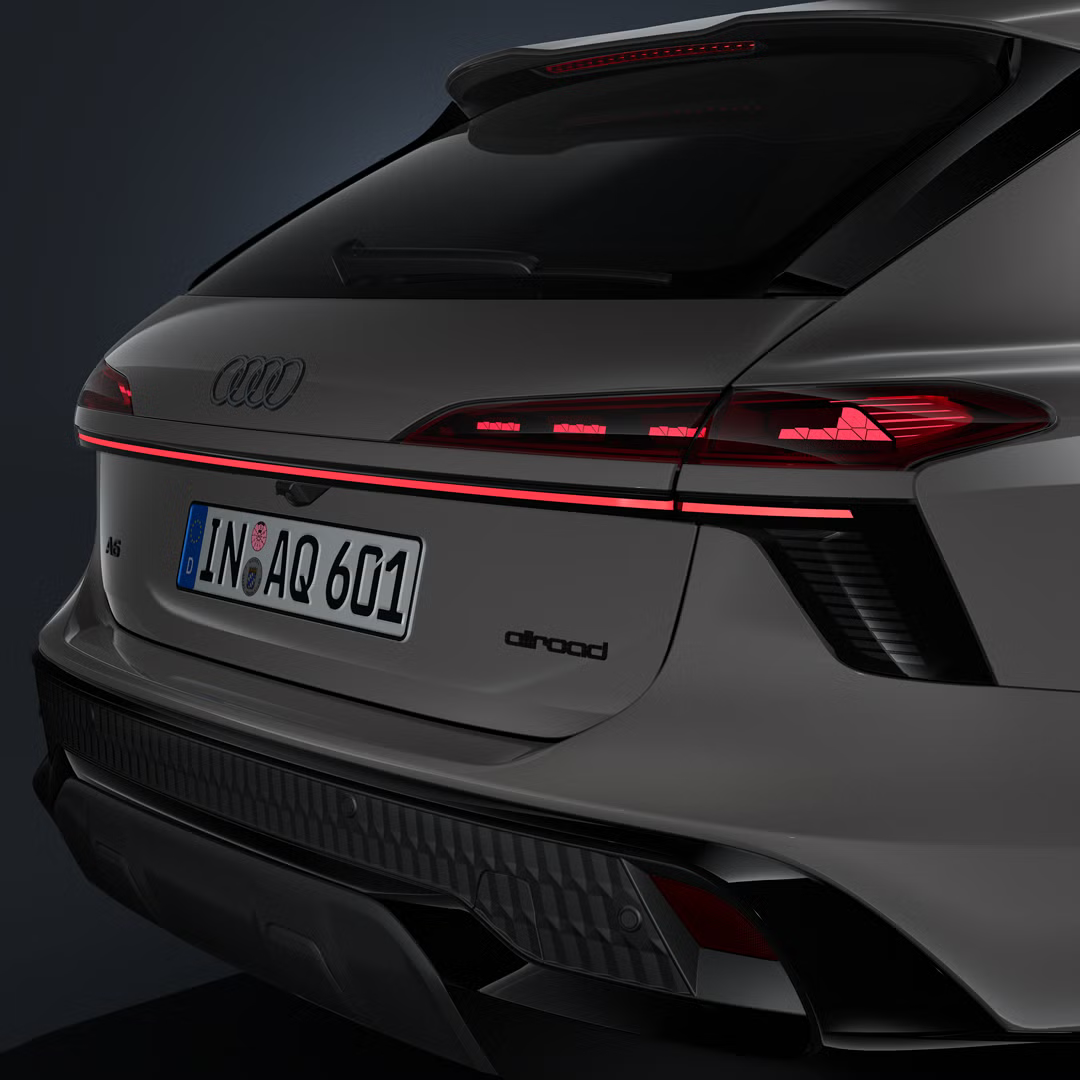 Poševni bližnji posnetek zadnjega dela vozila Audi A6 allroad s prikazom zadnjih luči in markantnega neprekinjenega svetlobnega segmenta.