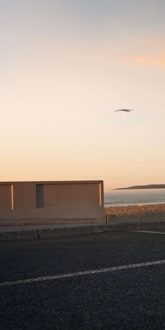 Temno moder Audi Q9 je parkiran ob obmorski promenadi, v ozadju pa je mirno morje in pastelno obarvano nebo ob sončnem zahodu.  