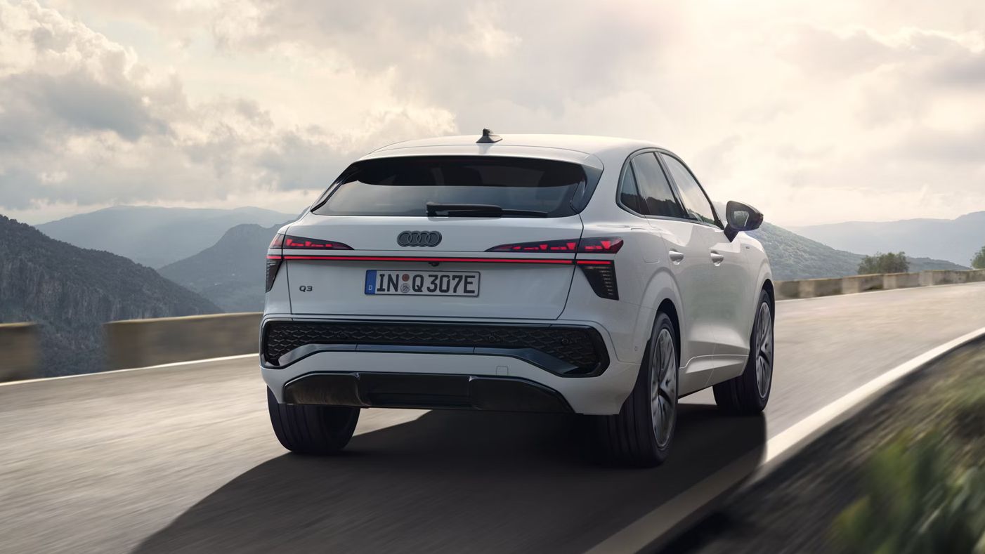 Beli Audi Q3 Sportback e-hybrid je prikazan med vožnjo po podeželski cesti v gorski pokrajini.