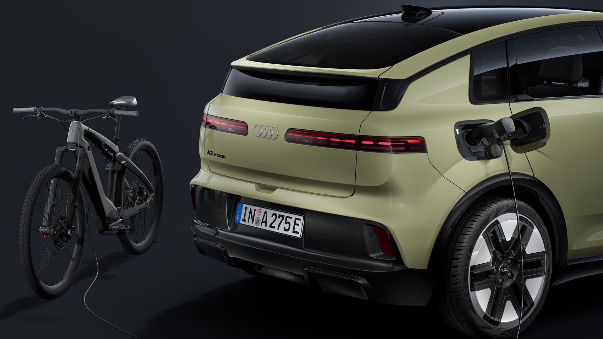 Bližnji posnetek zadnjega dela vozila. Na odprtem napajalnem priključku vozila Audi A2 e-tron je priključen električni kabel, ki polni e-kolo za vozilom.
